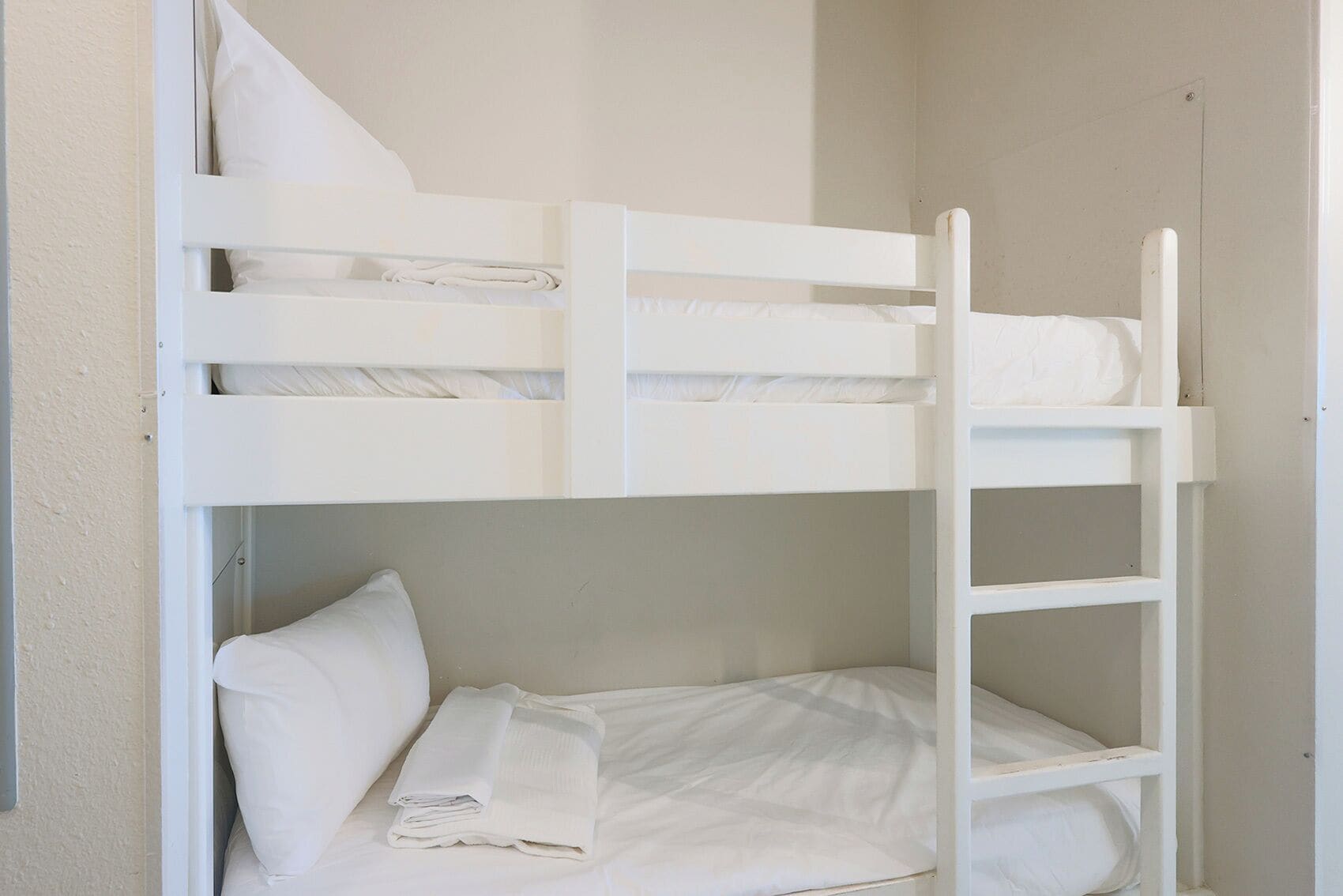 Una cama litera con ropa de cama blanca y una escalera.