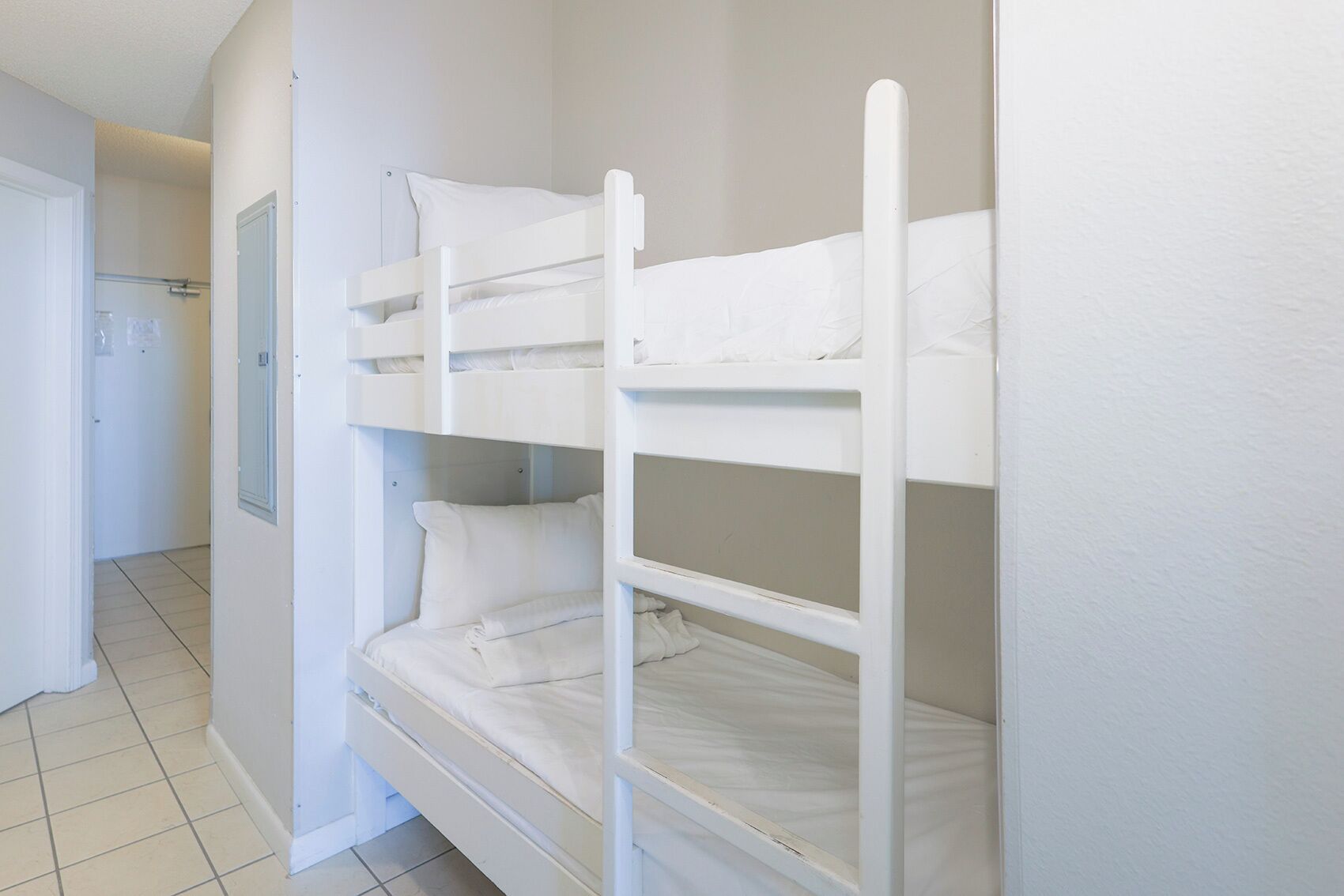 A bunk bed with white bedding in a room with white walls and a tiled floor.