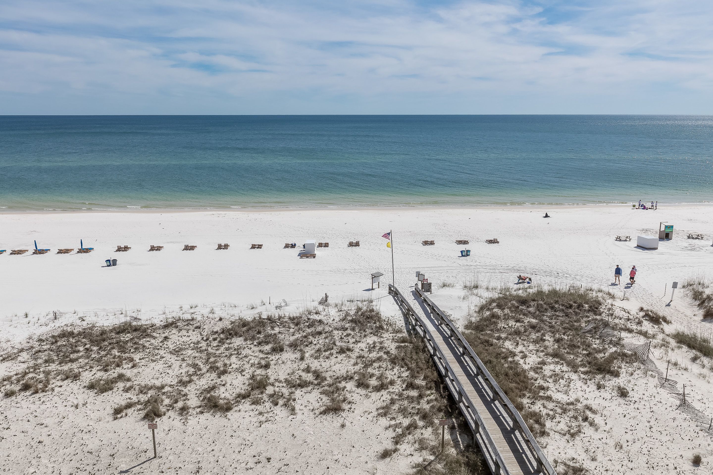 A beach with a wooden boardwalk, sandy dunes, and a clear view of the ocean.