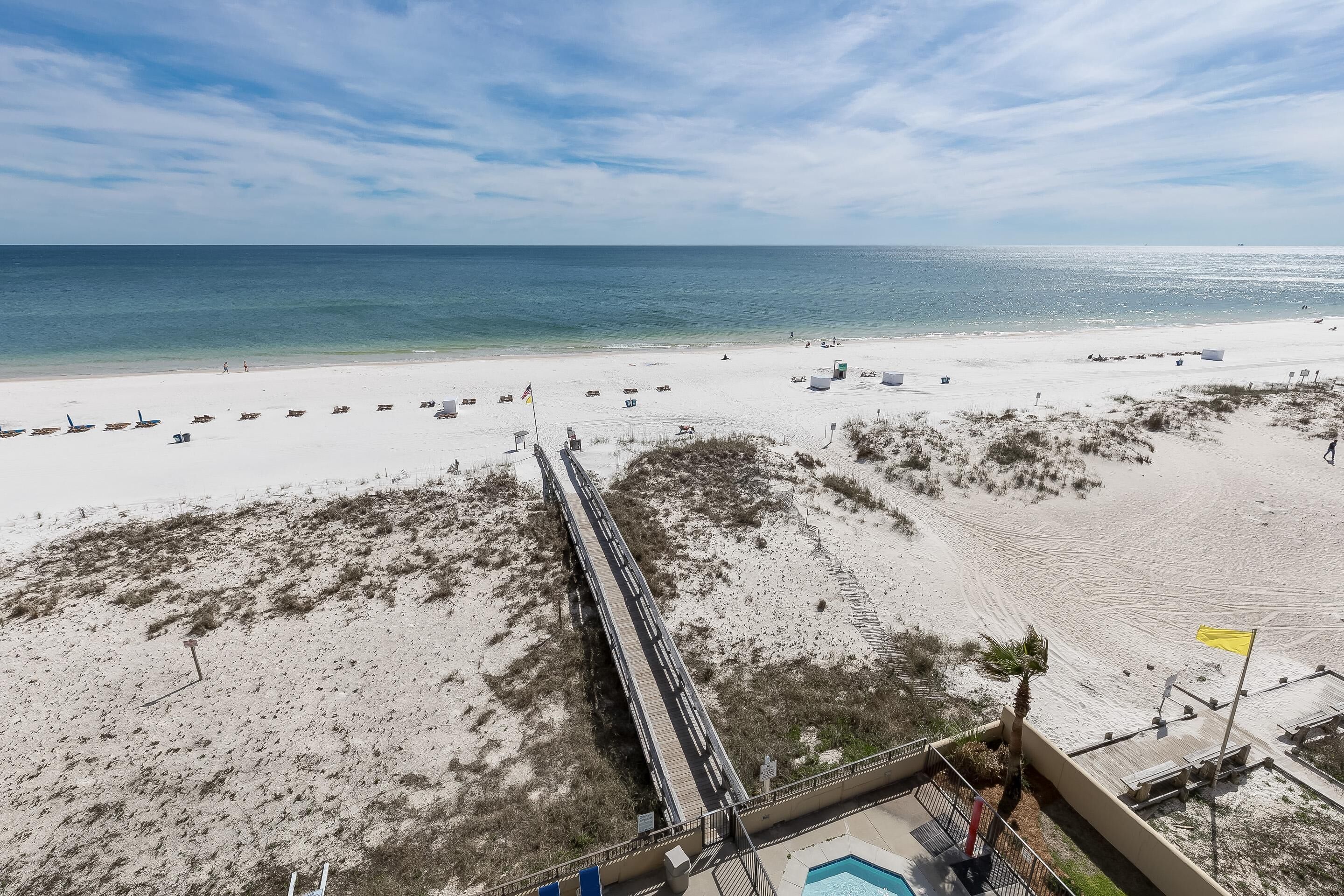 A beach with a long pier leading to the water, a sandy beach, and a clear sky.