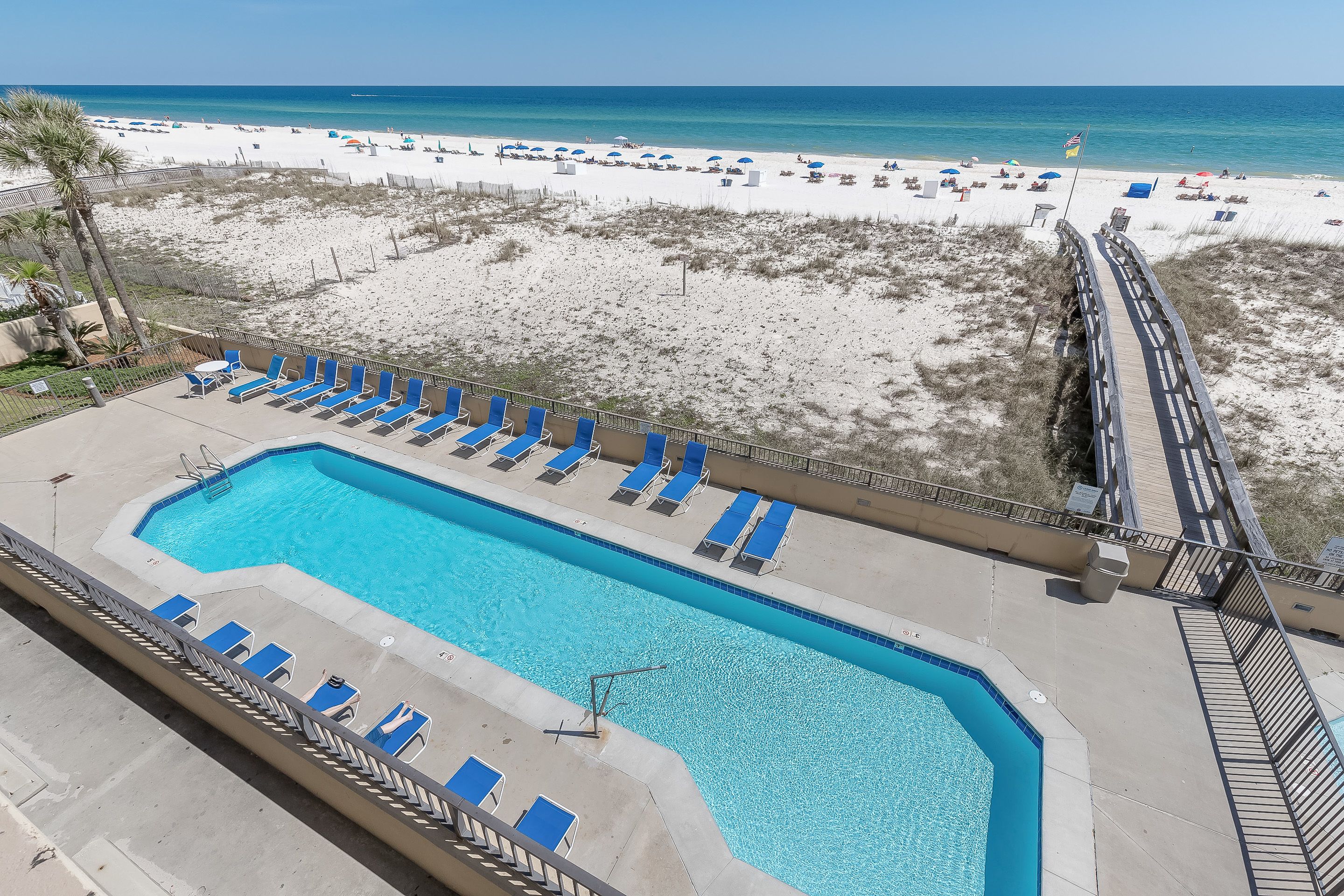 A pool area with blue lounge chairs and a view of the beach.