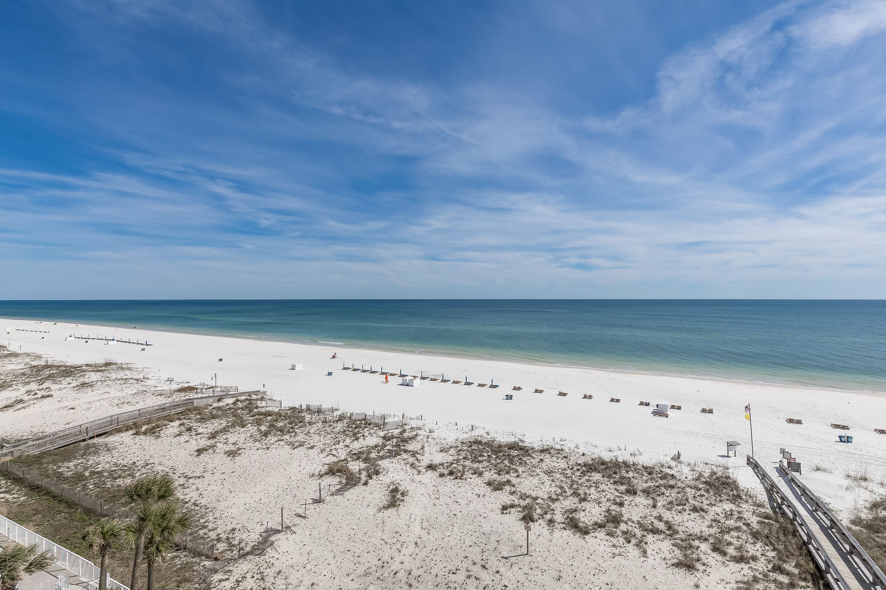 A beach with a wooden boardwalk, sandy dunes, and a clear blue sky.