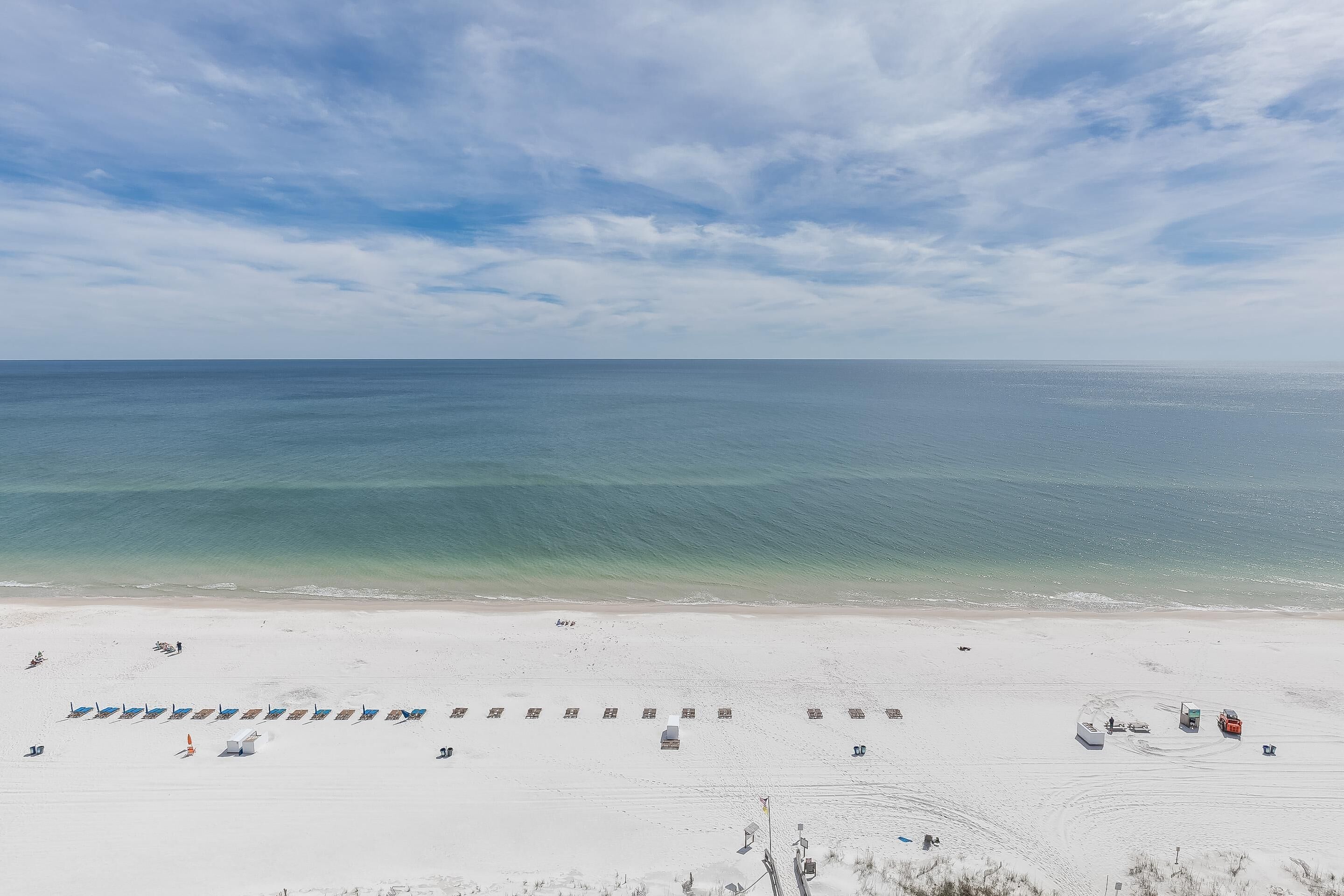 A beach with rows of beach chairs and umbrellas, a clear sky, and the ocean in the background.
