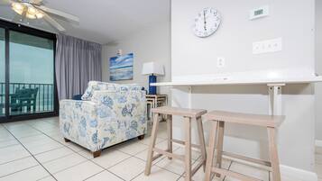 A room with a bed, a ceiling fan, a clock, and a digital thermostat.
