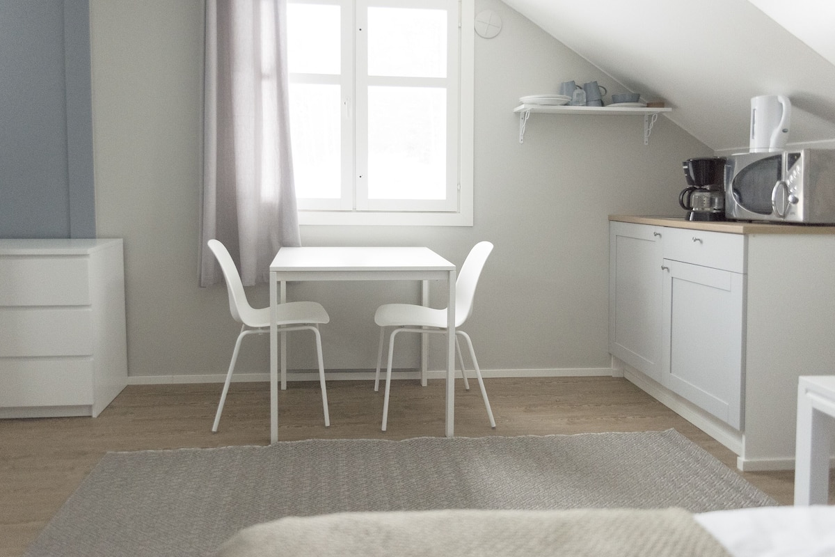 A small, bright room with a white table and two chairs, a microwave, and a shelf above the counter.