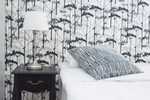 Una cama bien hecha con un almohadón a rayas y una lámpara de noche sobre una mesita de madera oscura.