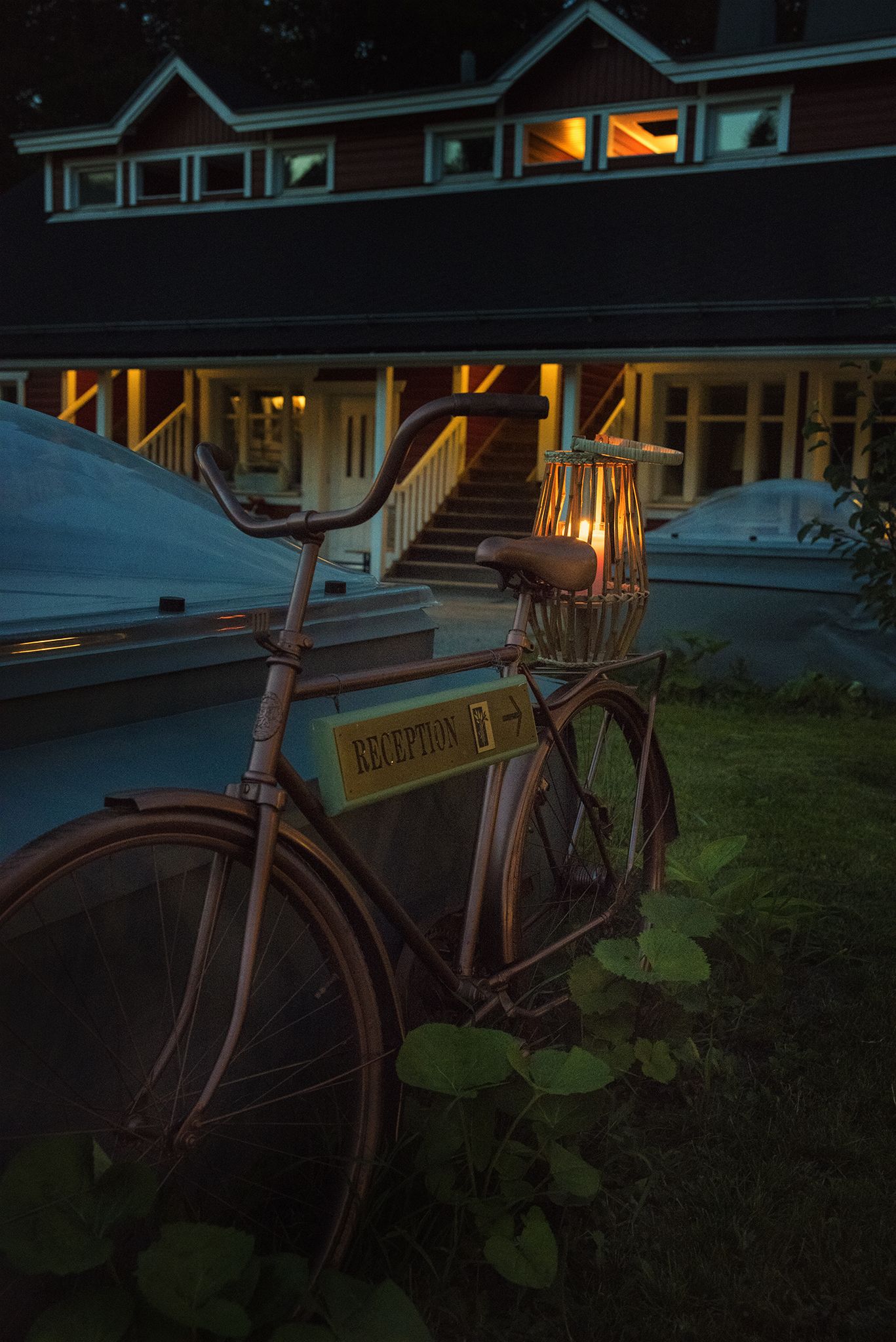 A bicycle with a basket and a sign labeled "RECEPTION" parked in front of a building with a staircase leading to a lit entrance.