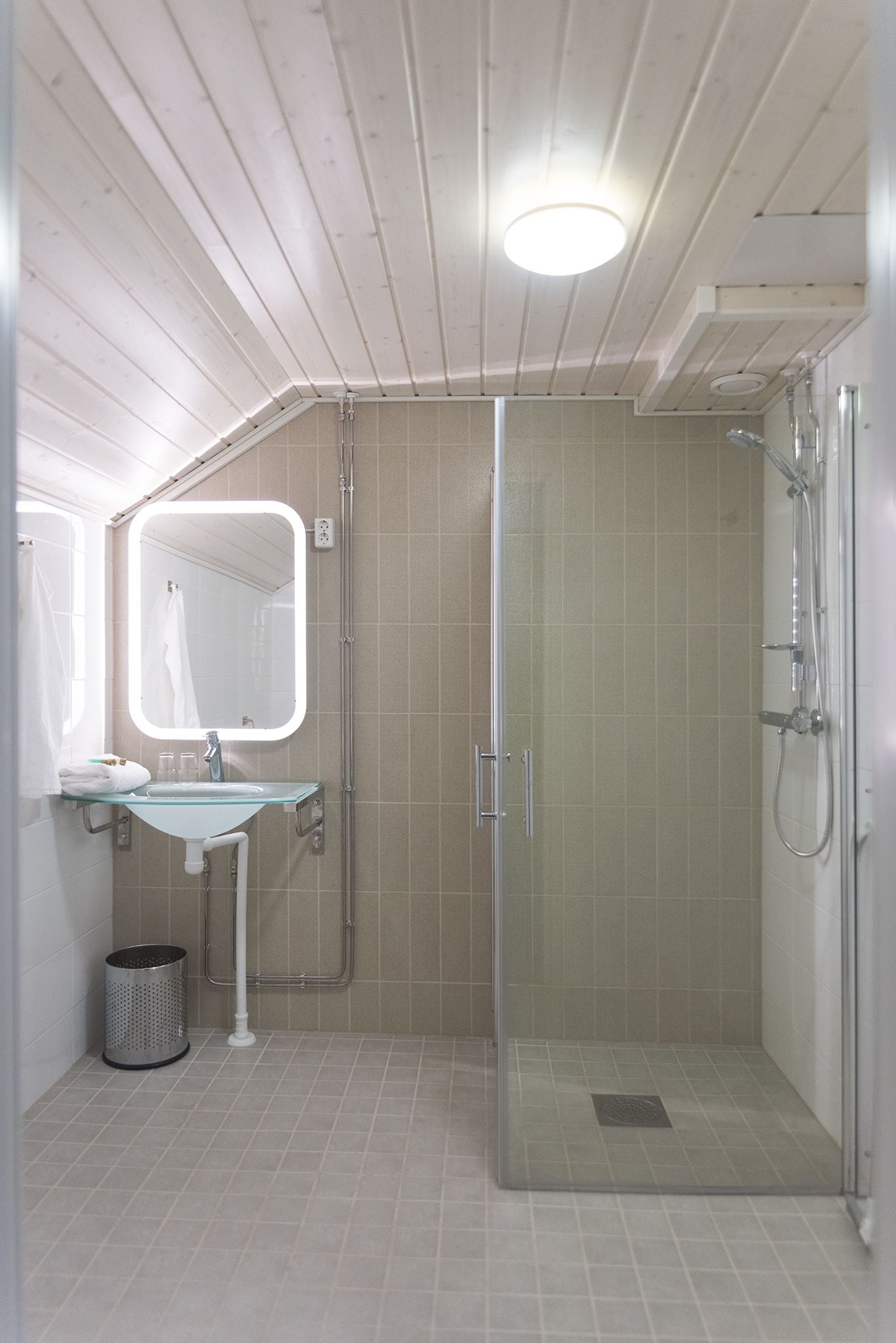 A bathroom with a glass-enclosed shower, a glass sink, and a mirror.