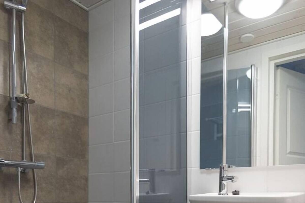 A bathroom with a glass shower enclosure, a sink, a mirror, and a trash can.