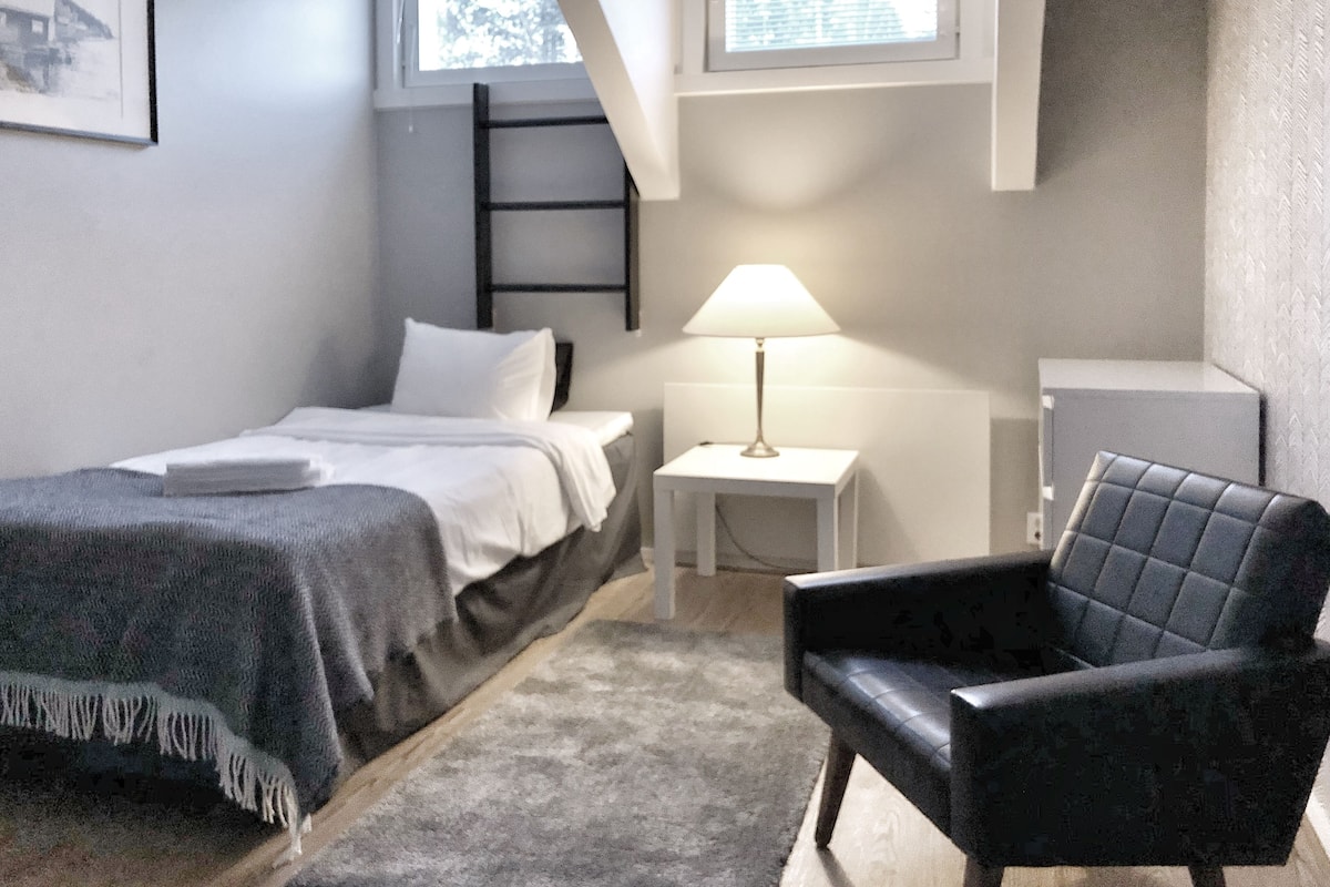 A bedroom with a bed, a chair, a nightstand, a lamp, and a window.