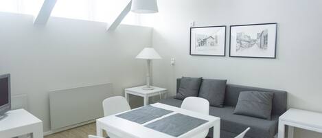 A modern living room with a white table, grey sofa, and two framed pictures on the wall.