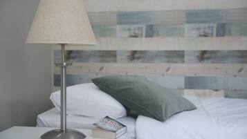 A neatly made bed with white linens, a green pillow, and a book titled "ONE OF A KIND" on a bedside table.