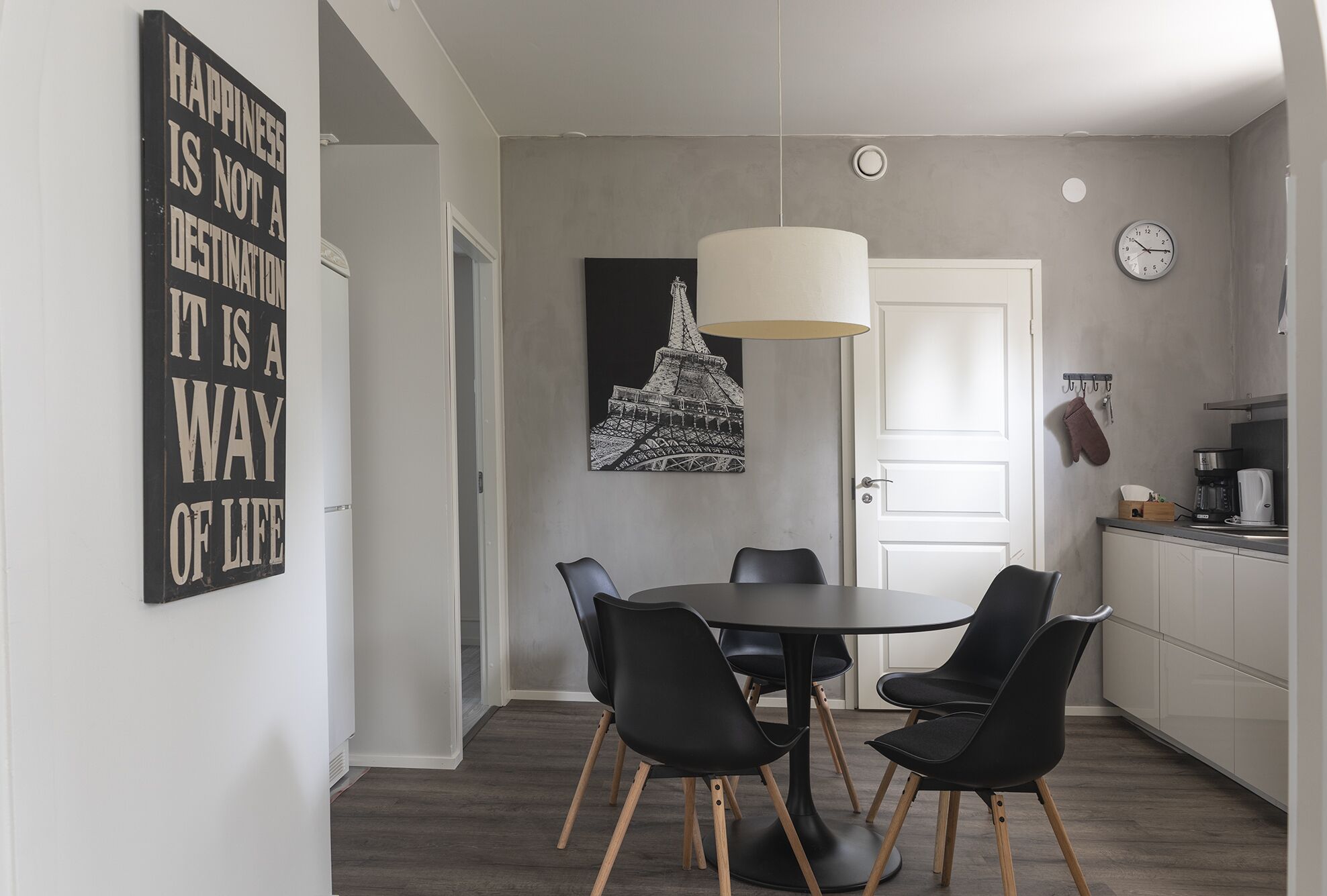 Una cocina moderna con comedor, que incluye una mesa negra con cuatro sillas, una lámpara colgante y un reloj en la pared.