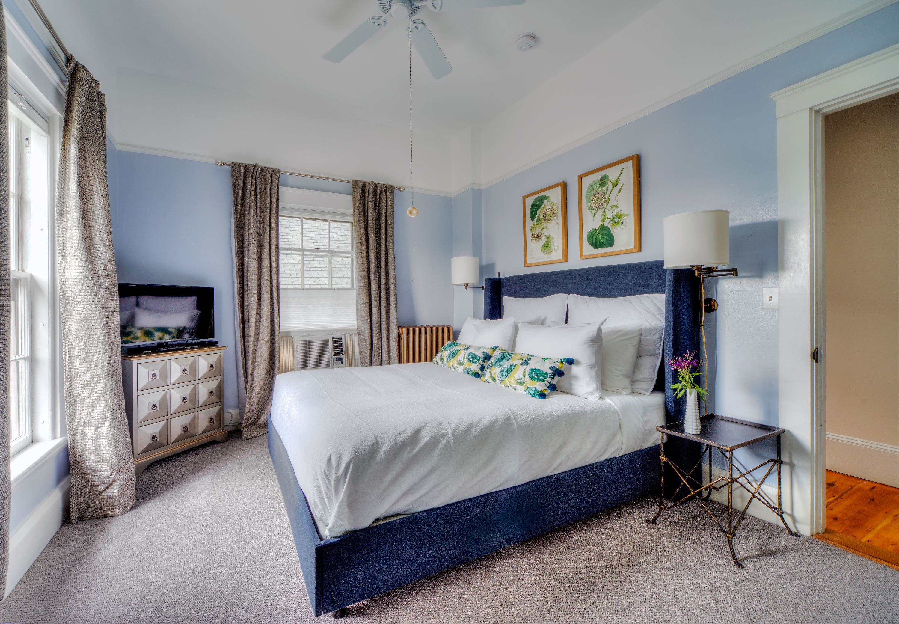A bedroom with a bed, a dresser, a nightstand, a lamp, and a ceiling fan.