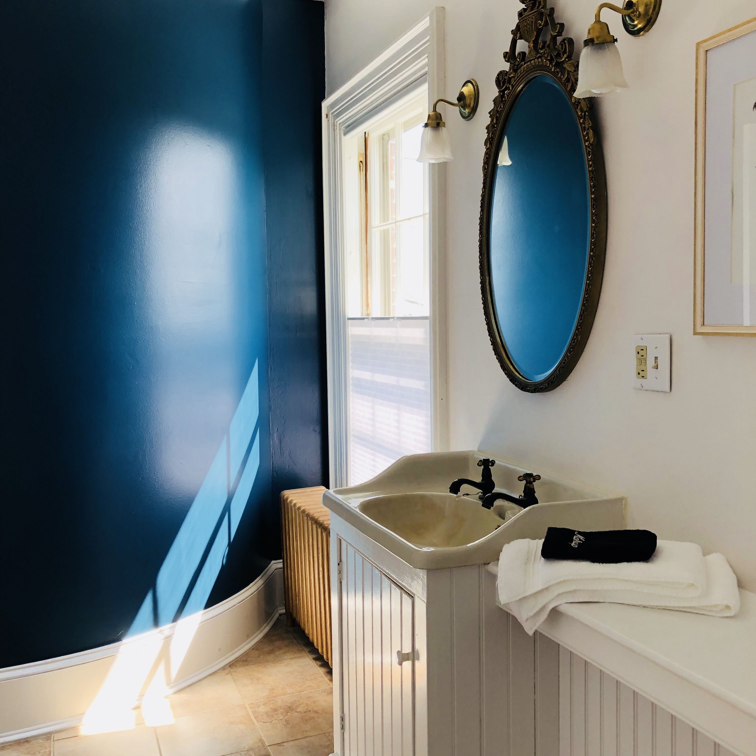 A bathroom with a blue wall, a white sink, and a mirror with a gold frame.