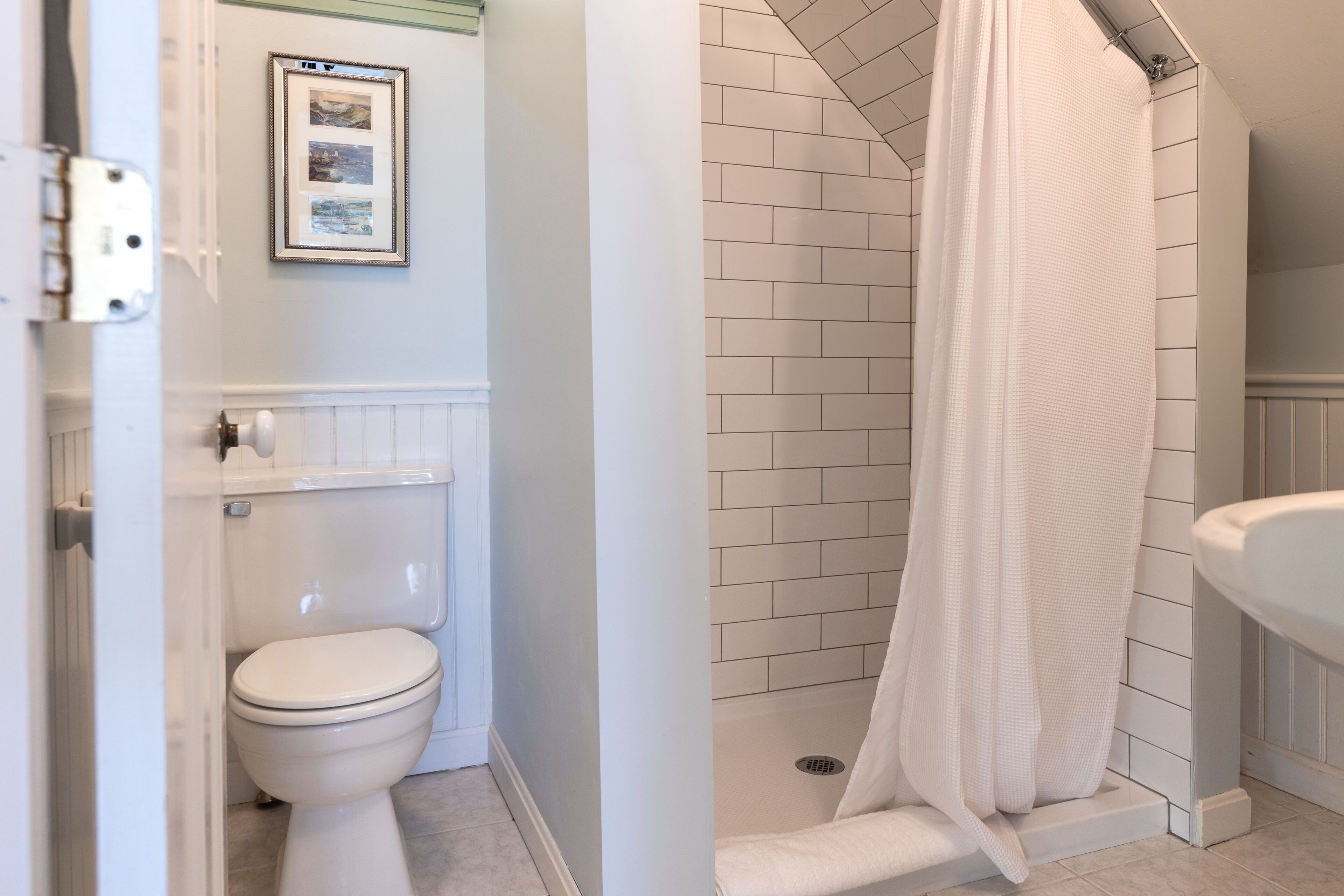 Ein Badezimmer mit Toilette, einem gerahmten Bild an der Wand und einer Dusche mit weißem Vorhang.
