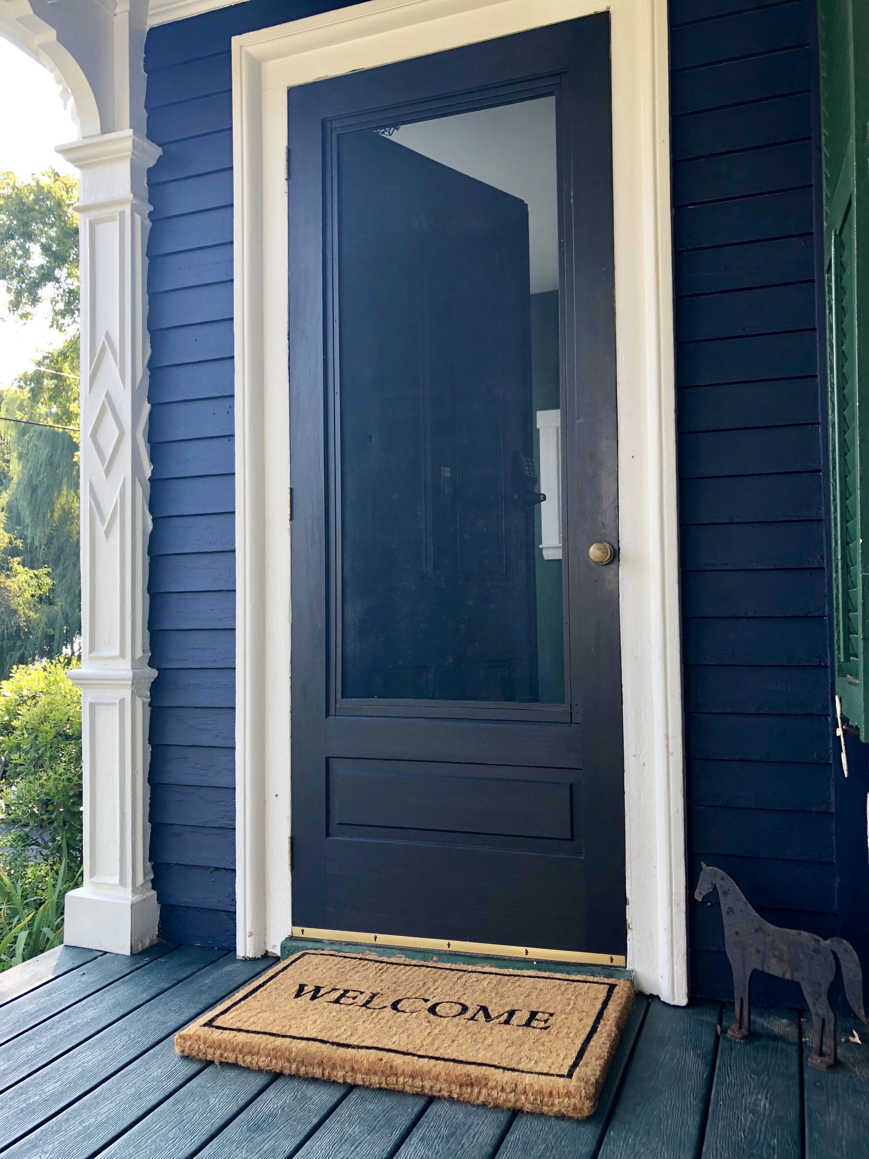A dark blue door with a white frame, a welcome mat, and a small horse decoration on the porch.