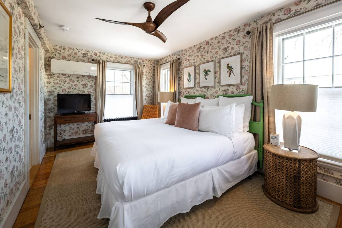 A bedroom with a large bed, a ceiling fan, a TV, and floral wallpaper.