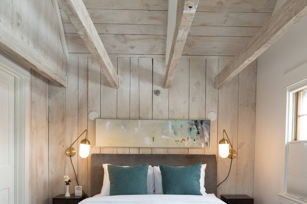 A bedroom with a large bed, wooden walls, two bedside tables, and wall-mounted lamps.