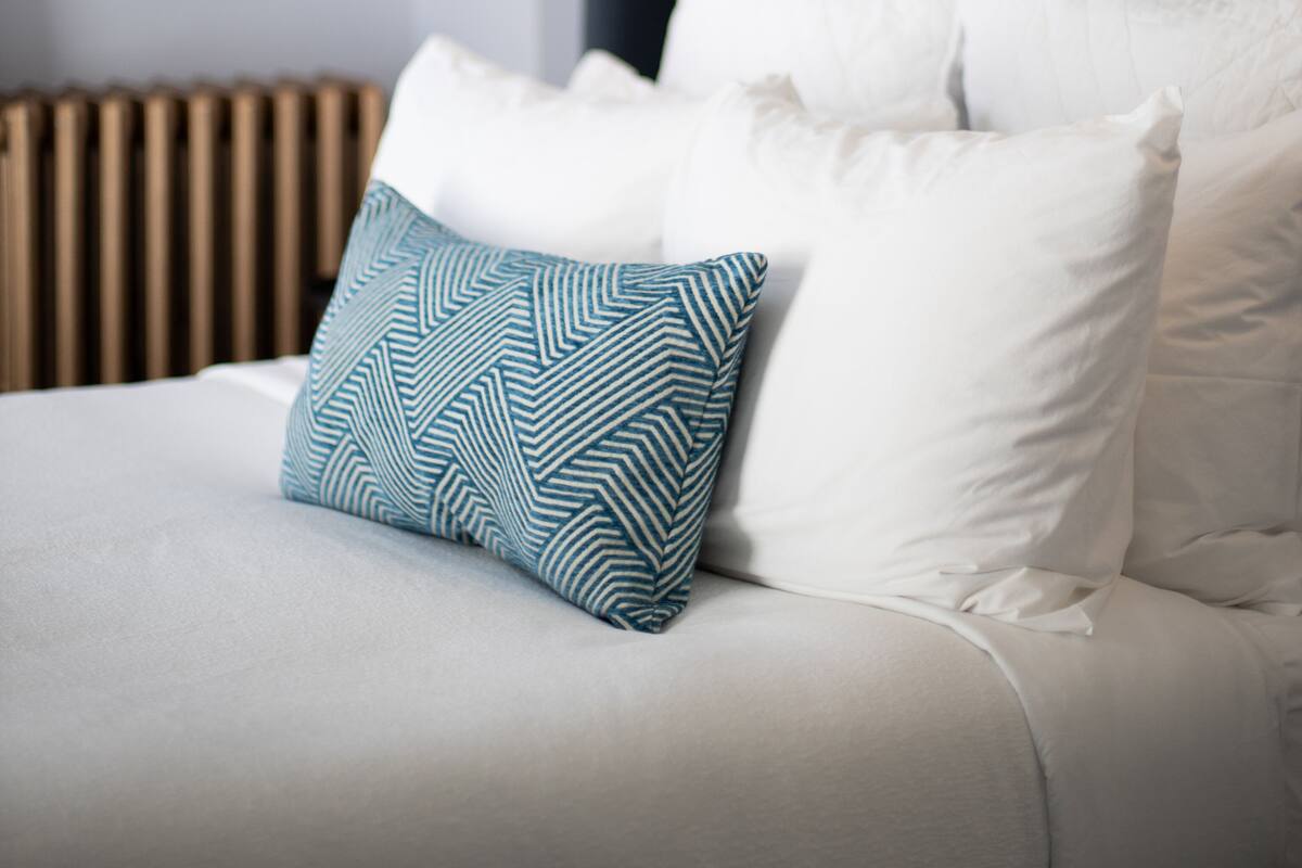 A neatly made bed with white and blue patterned pillows, a dark headboard, and a wall-mounted lamp.