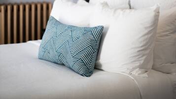 Una cama bien hecha con almohadillas blancas y azules estampadas, un cabecero oscuro y una lámpara fijada a la pared.