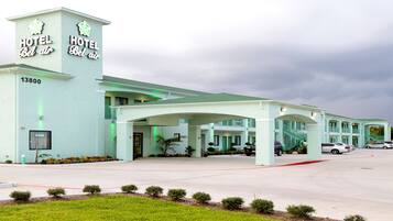 Un hotel con fachada verde claro, un letrero llamativo que dice "HOTEL Bel Air" y un estacionamiento con varios autos.