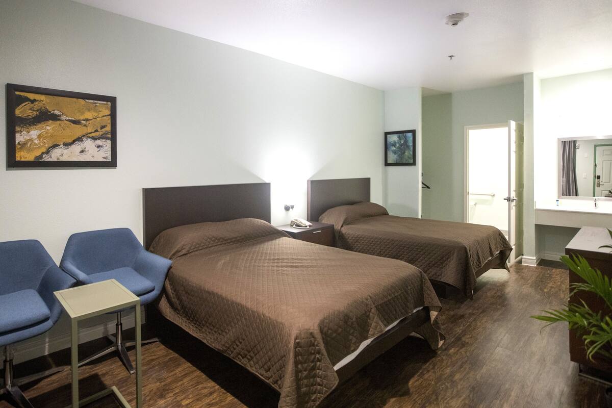Habitación de hotel con dos camas, un escritorio, una silla y una mesita de noche.