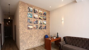 A modern living room with a wooden floor, a brown sofa, a desk with a chair, and a wall decorated with framed pictures. - Boots Travelers Lodge (Negombo)