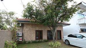 A residential house with a tiled roof, two air conditioning units, a white car parked in the driveway, and a small tree in the front yard. - Boots Travelers Lodge (Negombo)