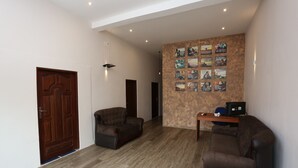A spacious hallway with a wooden door, two sofas, a small table with a computer, and a wall decorated with framed pictures. - Boots Travelers Lodge (Negombo)