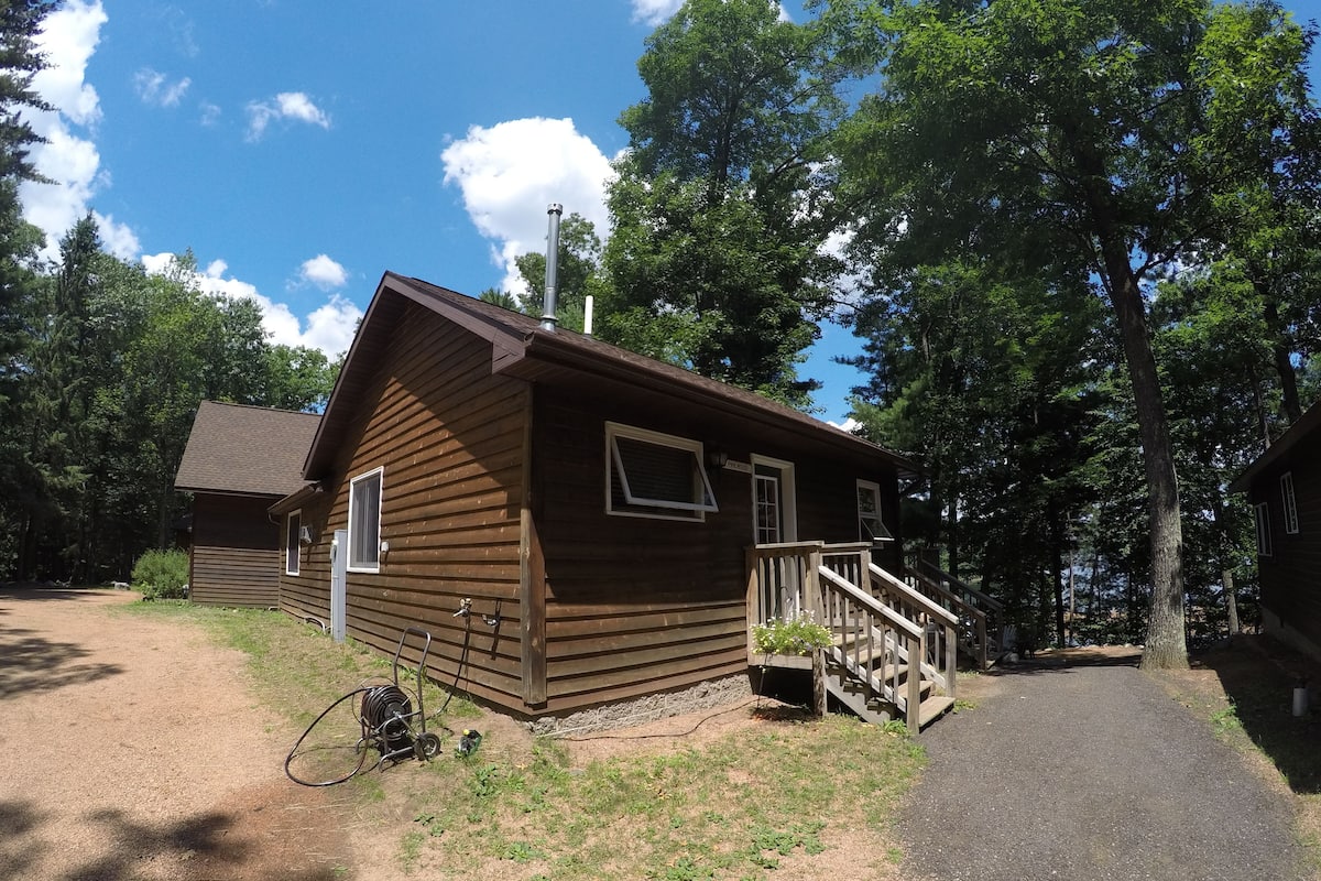 A small wooden cabin with a porch and a staircase leading up to the entrance.