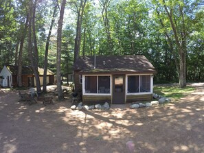 A small cabin with a porch, surrounded by trees. - Timber Bay Resort (Lac du Flambeau)