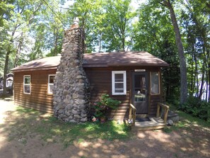 Una cabaña rústica con chimenea de piedra, fachada de madera y un pequeño porche.