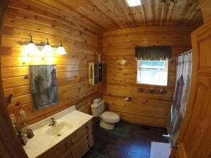 Baño de cabaña de madera con lavamanos, inodoro y ventana.