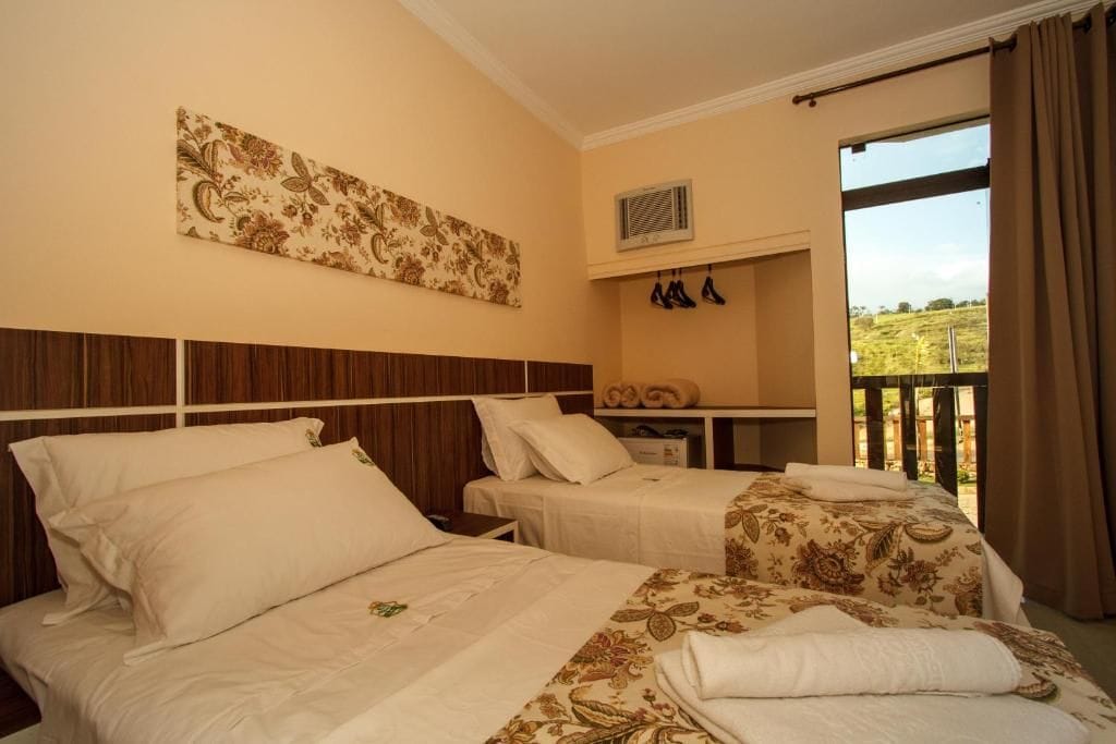 Habitación de hotel con dos camas, un ventanal con cortinas, una obra de arte en la pared y un zapatero.