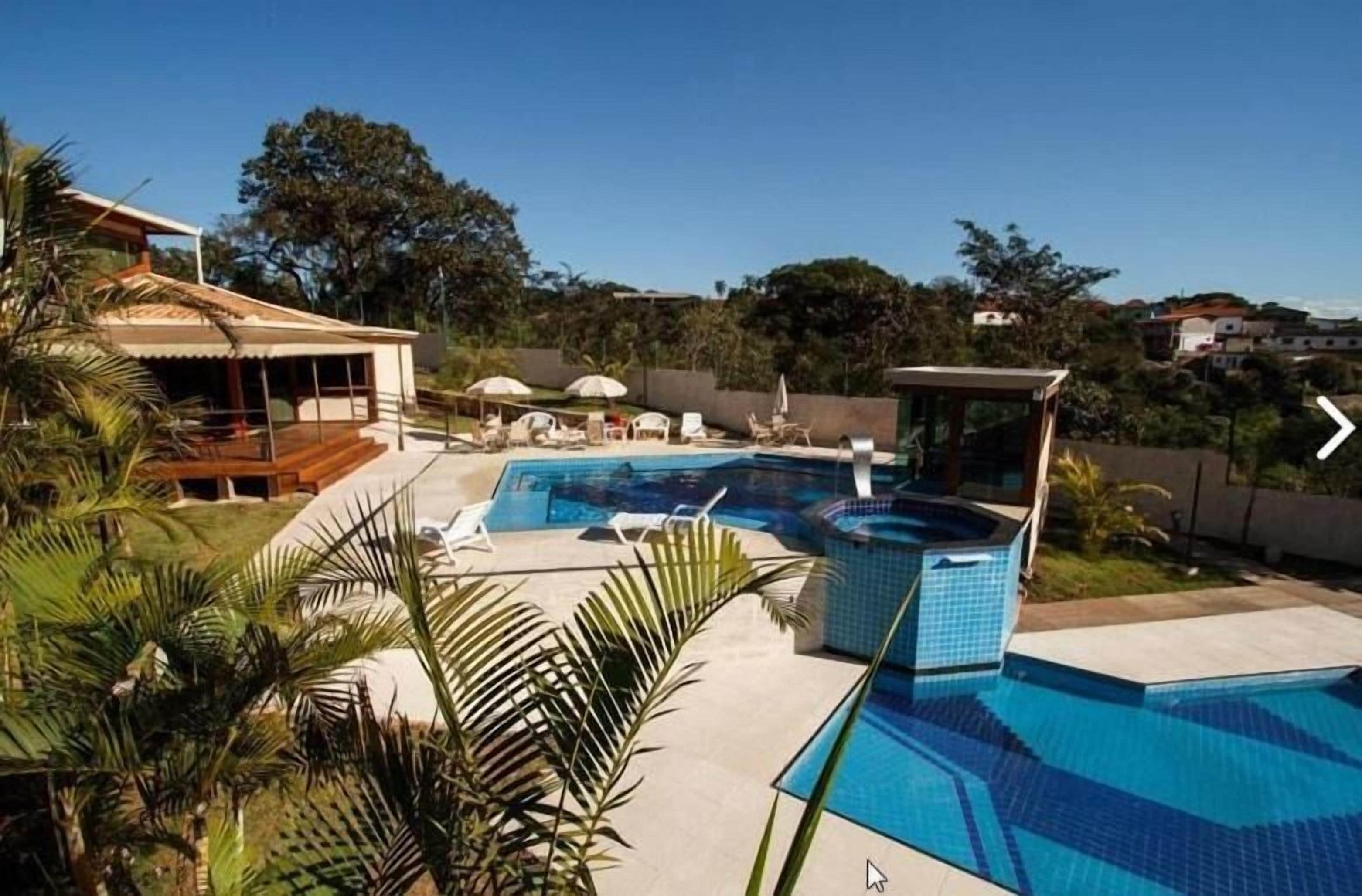 Una piscina con sillas de descanso y sombrillas, rodeada de palmeras y una casa.