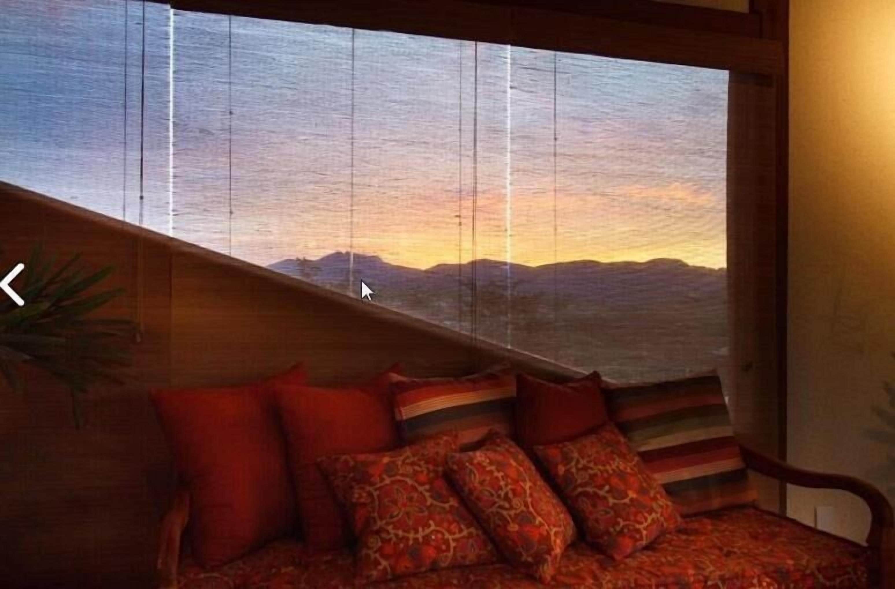 Una habitación con un amplio ventanal que da a un paisaje montañoso al atardecer.