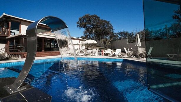 A swimming pool with a modern water feature, lounge chairs, and a building in the background. - Estrada Real Palace Hotel (Brumadinho)
