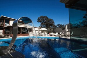 A swimming pool with a modern water feature, lounge chairs, and a building in the background. - Estrada Real Palace Hotel (Brumadinho)
