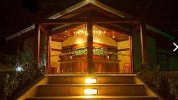 A wooden gazebo with a central seating area and a chandelier.