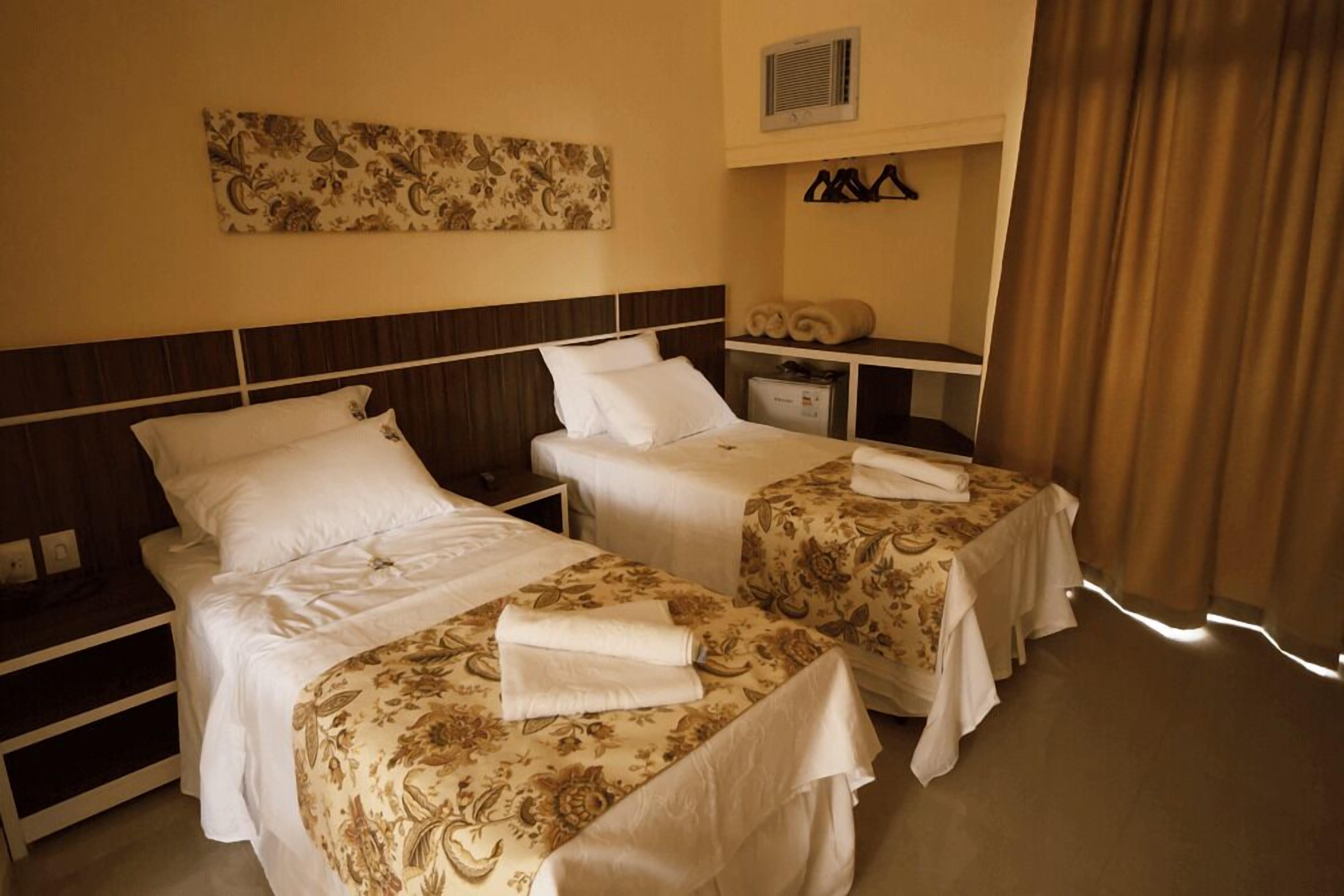 Ett hotellrum med två separata sängar, ett nattduksbord, ett skrivbord, en spegel och en väggmonterad luftkonditioneringsanläggning.