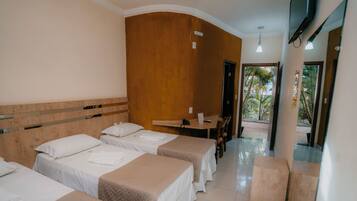 A hotel room with three beds, a wooden headboard, a desk with a chair, and a TV.