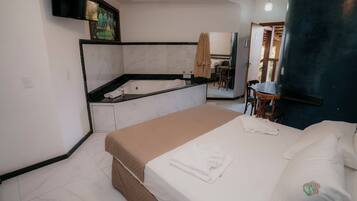 Quarto de hotel com cama, banheiro com banheira, televisão e área de refeições.