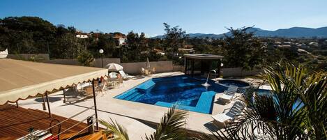 Una piscina en la azotea con sillones de descanso, una terraza de madera y vistas del paisaje circundante.