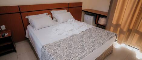Una habitación de hotel con cama, mesita de noche, armario y un refrigerador pequeño.