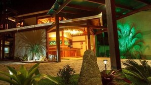 A hotel entrance with a reception desk, a stone pathway, and tropical plants. - Estrada Real Palace Hotel (Brumadinho)