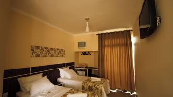 A hotel room with two beds, a flat-screen TV mounted on the wall, a ceiling fan, and a window with curtains.