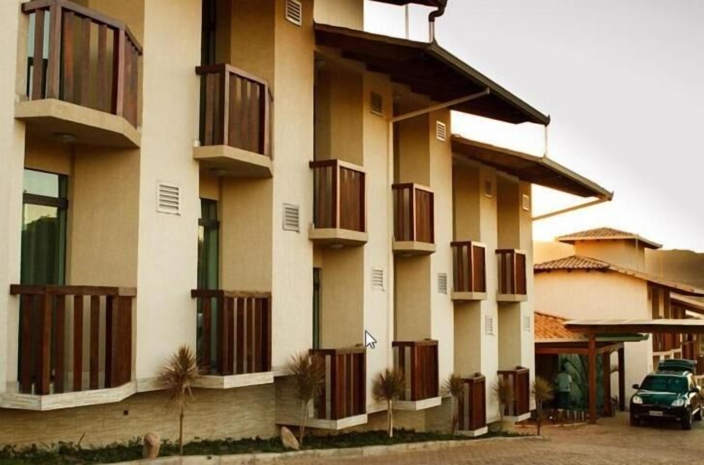 Un hotel de varios pisos con balcones, un estacionamiento techado y un coche estacionado al frente.