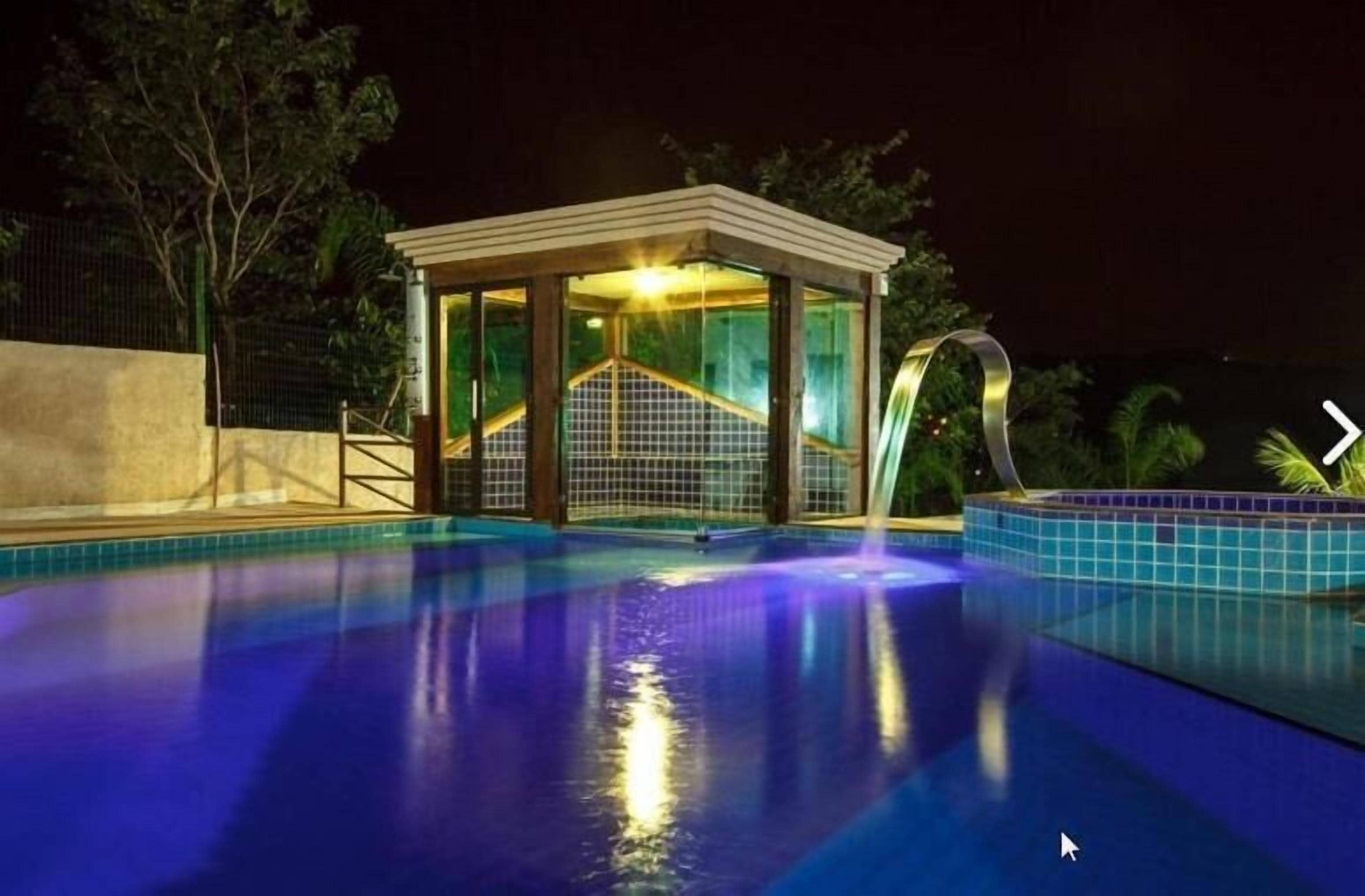 En swimmingpool med en glasad konstruktion runt om, omgiven av en låg mur och träd.