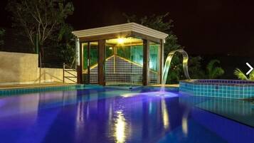 En swimmingpool med en glasad konstruktion runt om, omgiven av en låg mur och träd.